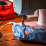 Sewing machine stitching edges of plastic fabric to form a durable tote bag